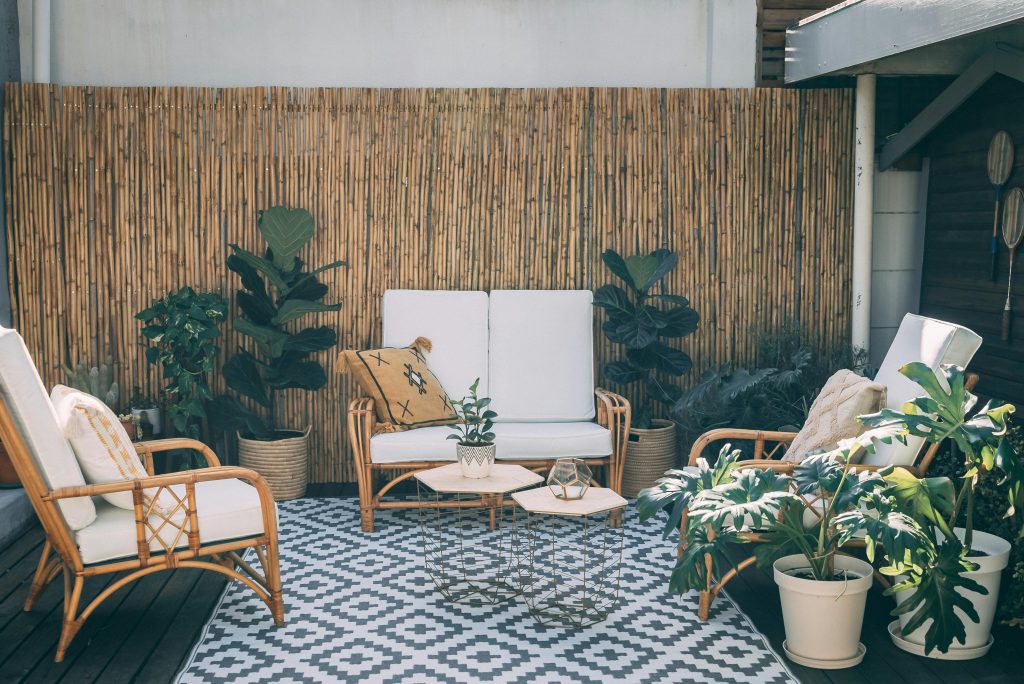 Serene outdoor patio featuring rattan furniture, potted plants, and bamboo decor.